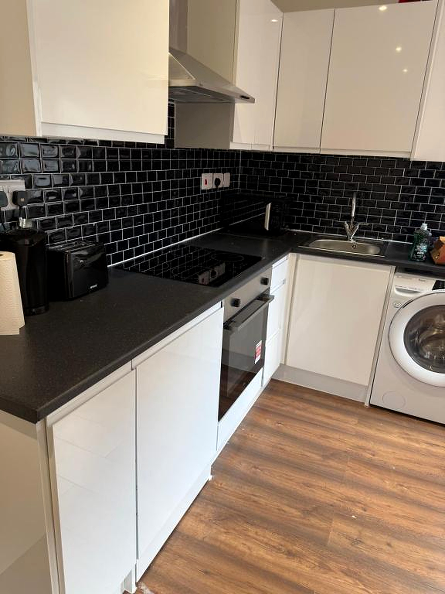 Fitted kitchen with white cabinets, oven, hob, sink and washing machine